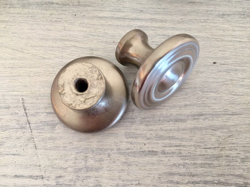 May include: Two silver cabinet knobs with a round base and a raised center. One knob has a smooth surface and the other has a textured surface.