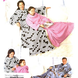 May include: Simplicity sewing pattern 2490 for a wearable blanket with sleeves. The package displays three variations: a black and white crossword puzzle print, a pink fabric with small dark patterns, and a blue fabric featuring a deer and forest print.