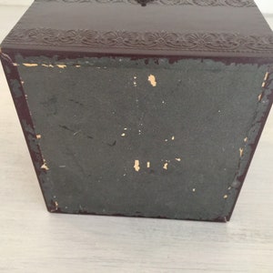 May include: A dark brown box with a decorative embossed design on the top and a plain bottom. The box is made of a sturdy material and has a slightly worn appearance.