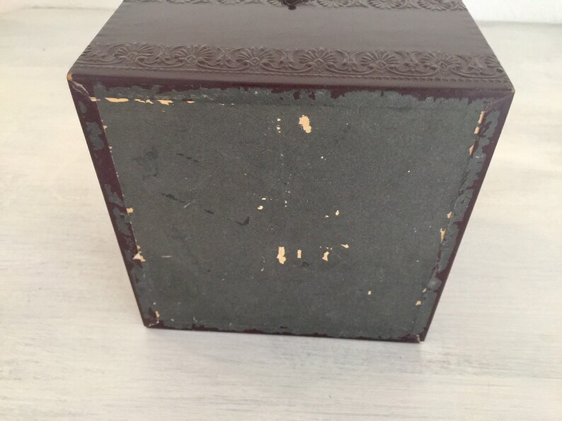 May include: A dark brown box with a decorative embossed design on the top and a plain bottom. The box is made of a sturdy material and has a slightly worn appearance.