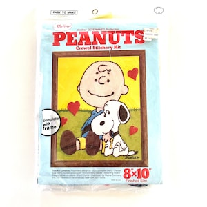 May include: A Peanuts crewel stitchery kit featuring Charlie Brown and Snoopy. The kit includes a preprinted design on 100% polyester fabric, embroidery yarn, a needle, a mounting board, and instructions. The finished size is 8x10 inches.