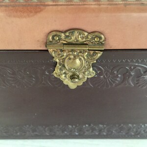 May include: A brown leather box with a decorative embossed design and a gold-toned metal clasp.