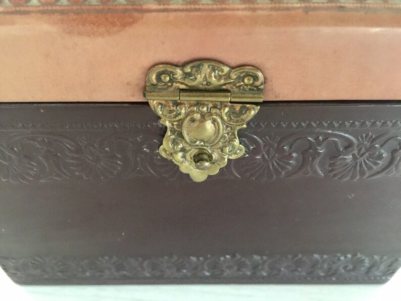 May include: A brown leather box with a decorative embossed design and a gold-toned metal clasp.