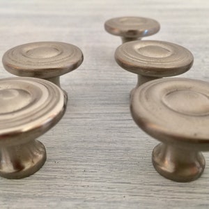 May include: Six silver cabinet knobs with a circular design and a raised center. The knobs have a smooth, polished finish.