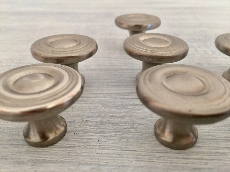 May include: Six silver cabinet knobs with a circular design and a raised center. The knobs have a smooth, polished finish.