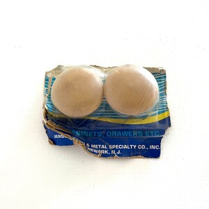 May include: Two round wooden knobs in a plastic package with blue and yellow text that reads "Cabinets, Drawers Etc. Jersey & Metal Specialty Co., Inc. Newark, N.J."