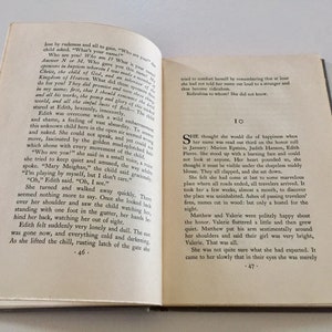 May include: A close-up of an open book with a white background. The text on the page reads, "She thought she would die of happiness when her name was read out third on the honor roll in January: Marion Epstein, Judith Hanson, Edith Pierre. She stood up with a burning face and could not look at anyone. Her heart pounded so, she thought it must be visible under the shapeless middy blouse. They all clapped, and she sat down."