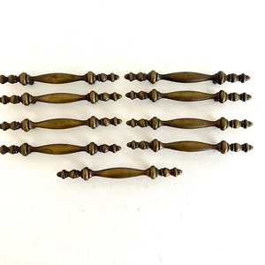 May include: Set of ten antique brass cabinet knobs with a decorative, ornate design. Each knob has a rounded, slightly curved shape with a series of small, raised bumps along the length.