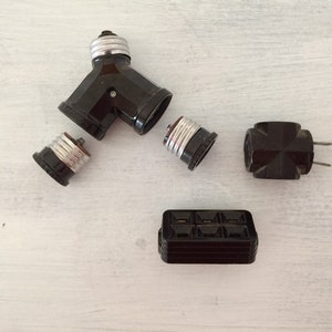 May include: A collection of vintage electrical components, including a Y-shaped light socket adapter, individual bulb sockets, a two-prong plug, and a fuse box. The components are dark brown and black, with silver-colored metal accents.