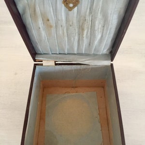 May include: An empty, brown wooden box with a light blue satin lining and a brass latch. The box is open and the inside is lined with a light brown paper.