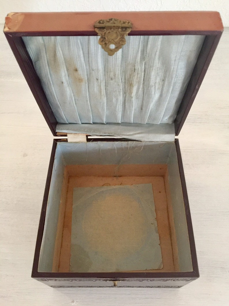 May include: An empty, brown wooden box with a light blue satin lining and a brass latch. The box is open and the inside is lined with a light brown paper.