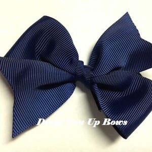 May include: A navy blue hair bow made from grosgrain ribbon. The bow is tied in a classic shape with two loops and a center knot.