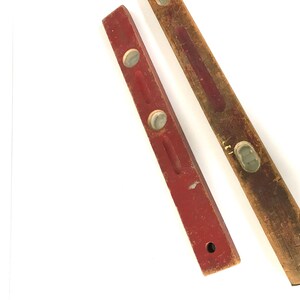 May include: Two wooden level tools. One is red with two white plastic bubbles. The other is brown with a white plastic bubble.