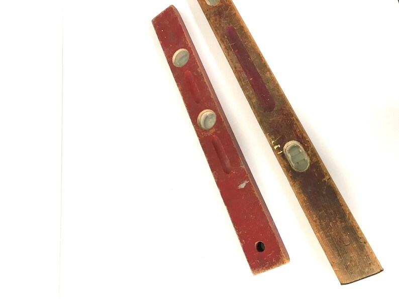 May include: Two wooden level tools. One is red with two white plastic bubbles. The other is brown with a white plastic bubble.