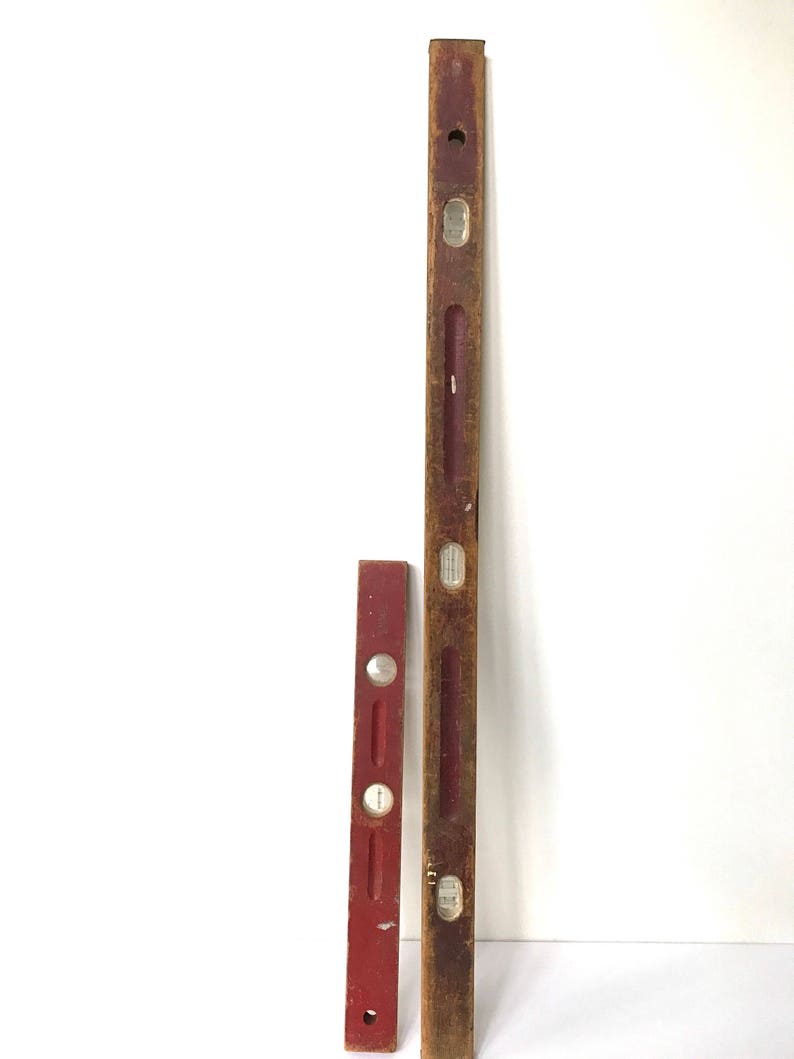 May include: Two vintage wooden levels, one red and one brown, with metal bubble vials. The levels are both about 18 inches long.