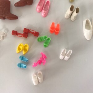May include: A collection of colorful plastic doll shoes, including boots, sandals, and flats. The shoes are in various colors, including pink, blue, yellow, green, and white.