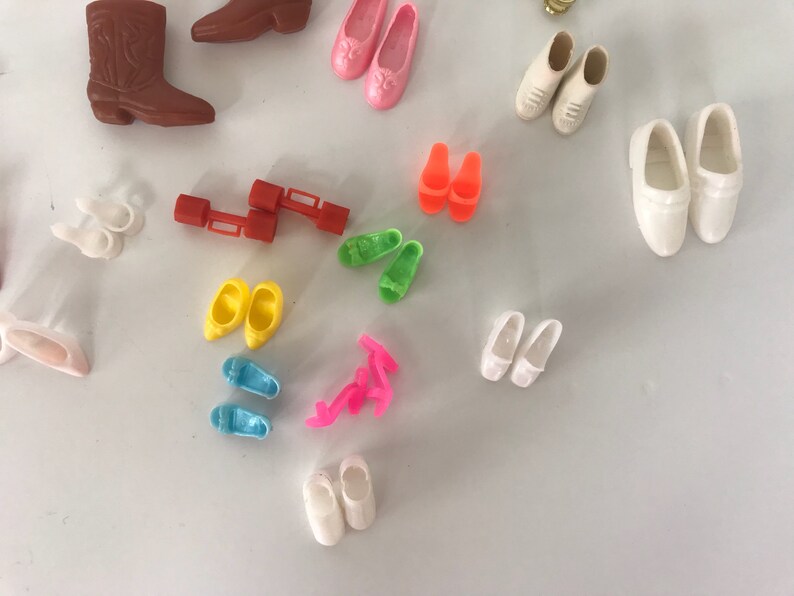 May include: A collection of colorful plastic doll shoes, including boots, sandals, and flats. The shoes are in various colors, including pink, blue, yellow, green, and white.