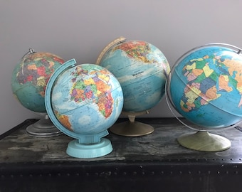 Op de afbeelding: Vier vintage globes van de wereld, elk met een andere basis en standaard. De globes zijn blauw met kleurrijke continenten en oceanen. De globes zijn gerangschikt op een donker houten oppervlak.