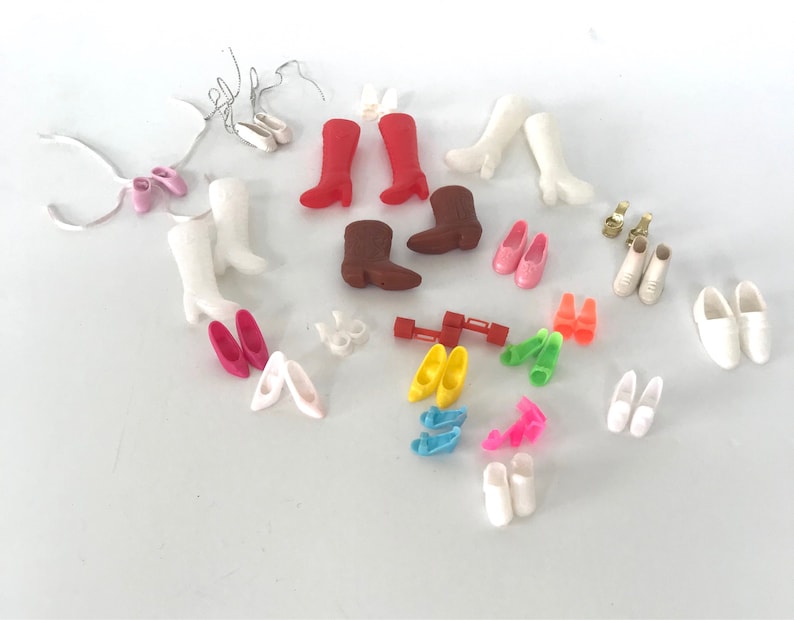 May include: A collection of various doll shoes and boots in different colors, including white, pink, red, brown, yellow, blue, and green. The shoes are made of plastic and are in various styles, including flats, heels, boots, and sandals.