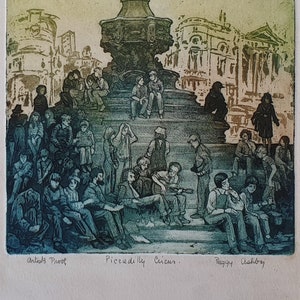 Op de afbeelding: Een groene en blauwe ets van Piccadilly Circus in Londen, Engeland. De afbeelding toont een standbeeld van Eros bovenop een fontein, met mensen die op de trappen eronder zitten. De tekst "Artists Proof", "Piccadilly Circus" en "Peggy Ashbey" is zichtbaar onderaan de afbeelding.