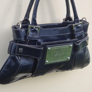 May include: A dark blue patent leather handbag with silver hardware and a silver nameplate that reads "Guess" on the front.
