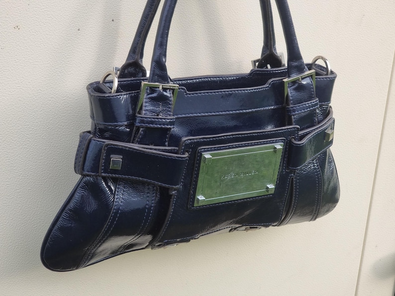May include: A dark blue patent leather handbag with silver hardware and a silver nameplate that reads "Guess" on the front.