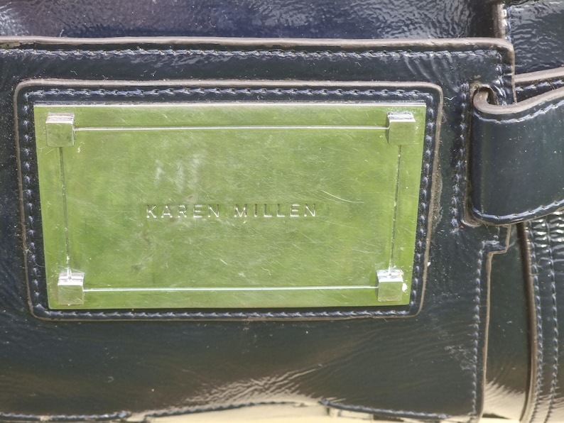 May include: A black leather handbag with a silver metal plate that reads "KAREN MILLEN".