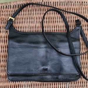 Könnte beinhalten: Eine schwarze Lederschultertasche mit einem langen Riemen. Die Tasche hat einen Klappverschluss und der Markenname "JUDESIGN" ist auf der Vorderseite geprägt.