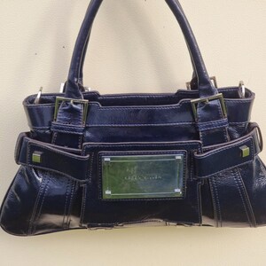 May include: A dark blue leather handbag with silver hardware and a rectangular nameplate that reads "Karen Millen".