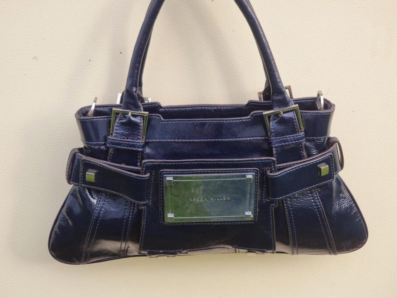 May include: A dark blue leather handbag with silver hardware and a rectangular nameplate that reads "Karen Millen".