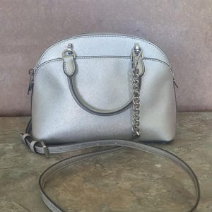 Bolso Emmy Dome de piel saffiano plateada de Michael Kors, bolso plateado con asa superior, bolso bandolera tipo cartera, bolso de piel con asa superior y cadena.
