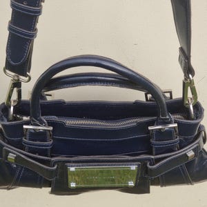 May include: A dark blue leather handbag with silver hardware and a top zipper closure. The bag has a top handle and a shoulder strap.