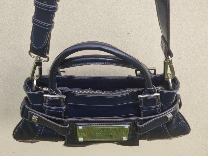 May include: A dark blue leather handbag with silver hardware and a top zipper closure. The bag has a top handle and a shoulder strap.