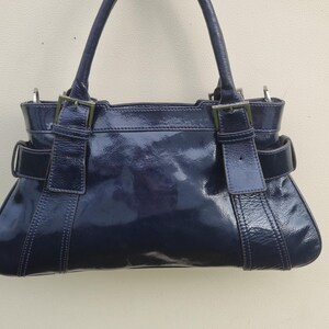 May include: A dark blue patent leather handbag with silver hardware and a top handle.