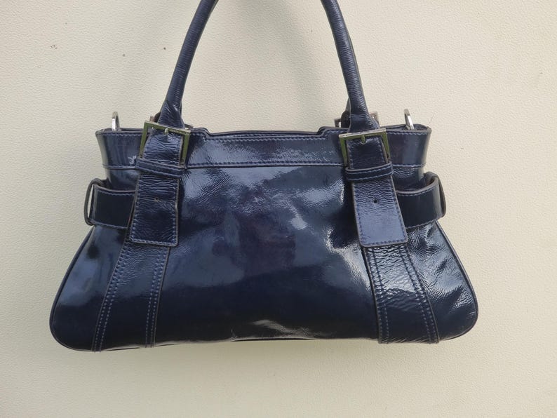 May include: A dark blue patent leather handbag with silver hardware and a top handle.