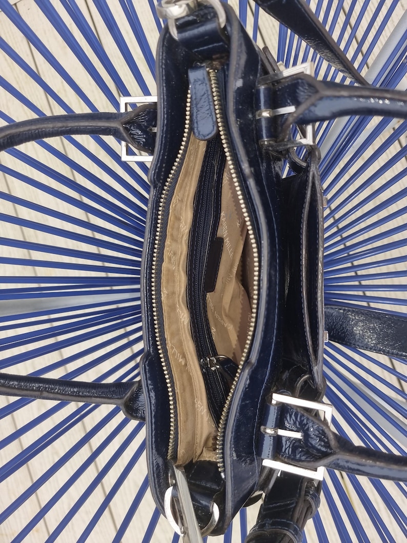 May include: A black patent leather handbag with silver hardware and a zipper closure. The bag has a top handle and a shoulder strap.