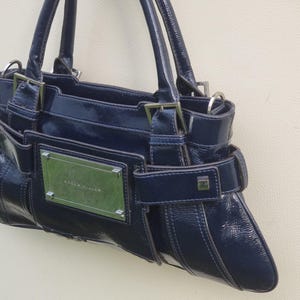 May include: A dark blue leather handbag with a silver buckle and a silver nameplate that reads "Karen Millen".