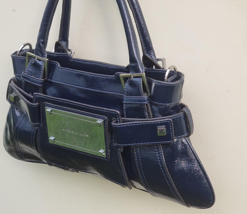 May include: A dark blue leather handbag with a silver buckle and a silver nameplate that reads "Karen Millen".