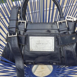 May include: A dark blue patent leather handbag with silver hardware and a silver plaque that reads "Karen Millen".