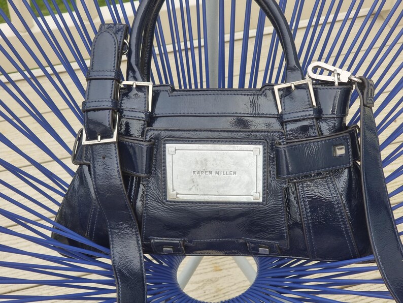 May include: A dark blue patent leather handbag with silver hardware and a silver plaque that reads "Karen Millen".