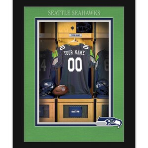 May include: A framed print of a Seattle Seahawks locker room with a jersey hanging on a hook. The jersey is green and blue with the words "YOUR NAME" and the number "00" on the back. The print is surrounded by a green mat and a black frame.