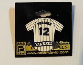 May include: A white and black striped baseball jersey with the word "Colorado" and the number "12" on the back. The jersey has a black banner with the word "Yankees" on it.