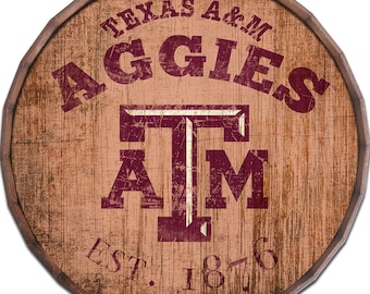 Könnte beinhalten: Ein braunes und weißes Holzschild mit dem Text "Texas A&M Aggies" und einem maroonfarbenen "TAM"-Logo mit weißem Umriss. Das Schild enthält auch den Text "Est. 1876".