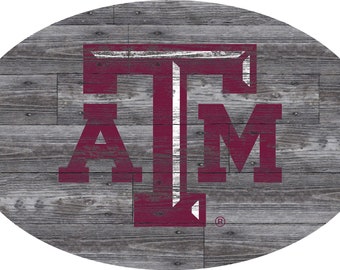 Könnte beinhalten: Ein "A&M"-Logo in Maroon und Weiß auf einem grauen Holzmaserungshintergrund. Das Logo ist im Used-Look gehalten, wobei die Buchstaben so aussehen, als wären sie auf das Holz gemalt.