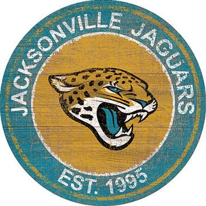 May include: A circular wooden sign with a distressed teal blue background and a gold circle in the center. The gold circle features a white and gold jaguar head with a teal blue tongue. The text "JACKSONVILLE JAGUARS EST. 1995" is written in white around the gold circle.