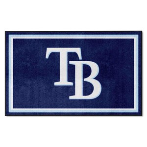 May include: A rectangular area rug featuring a deep navy blue background with a large, white, stylized TB logo centered in the middle. The rug is framed by a thin black outer border and a light blue inner border that outlines the entire design.