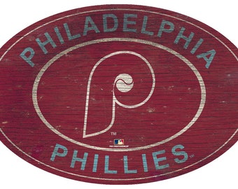 May include: Oval wooden sign featuring the Philadelphia Phillies logo. The sign has a distressed, vintage look with a red background and the team's logo in white and blue. The text "PHILADELPHIA PHILLIES" is displayed.