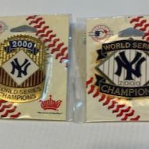 May include: Two gold and blue New York Yankees World Series Championship pins from 2000. The pins are on a red and white baseball-themed background.