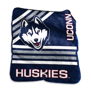 May include: A navy blue and white Huskies blanket featuring the UConn Husky logo. The blanket has a distressed look with white and gray stripes and the word "Huskies" in white lettering. The word "UCONN" is printed vertically in white.