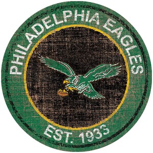 May include: A green and black circular sign with the words "Philadelphia Eagles" and "Est. 1933" in white lettering. The sign features a distressed wood-like texture and a green eagle with a football in its talons.